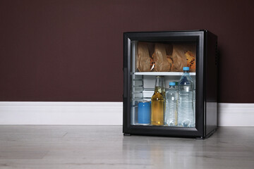 Mini bar filled with food and drinks near brown wall indoors, space for text