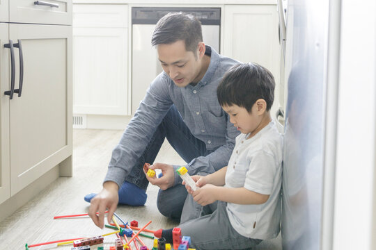 Father and son playing with plastic blocks on kitchen floor