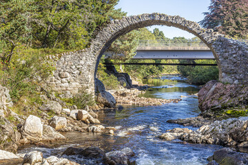 Fototapeta na wymiar The remains of the Old Packhorse Bridge built in 1717 and the more modern road bridge over the River Dulnain in the village of Carrbridge, Highland, Scotland UK.