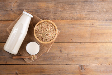 Vegan non diary buckwheat milk in bottle with buckwheat groats on a wooden background. Vegan buckwheat drink is plant based alternative milk . Veggies healthy milk product, copy space, top view