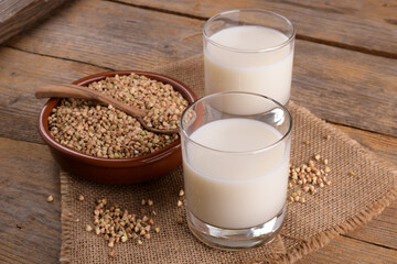 Vegan non diary buckwheat milk in glasses with buckwheat groats in a clay bowl on a wooden background. Vegan buckwheat drink is plant based alternative milk . Veggies healthy milk product, copy space