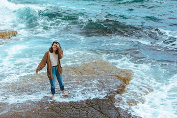 Fototapeta premium woman walking by rocky beach in wet jeans barefoot