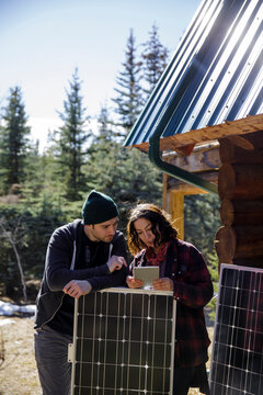 Couple installing solar panels and rain barrel on cabin