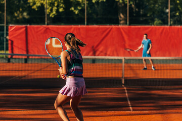 Fototapeta premium View from the back of a young female paying tennis on a court outside