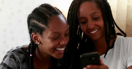 Two girls laughing looking at cellphone device. Black ethnicity girlfriends