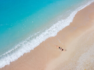 overhead view of woman in black swimsuit sunbathing at sea shore