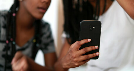 Two black girls looking at cellphone screen laughing together. African American ethnicity