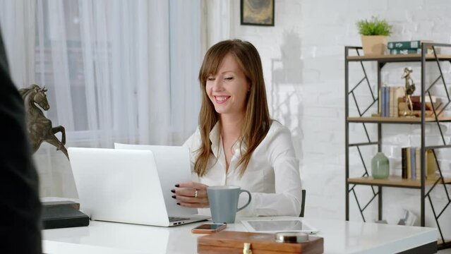 Young business woman working at desk with laptop computer in home office. Getting document looking relieved.