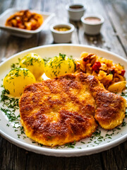 Breaded fried pork chop with boiled potatoes and cabbage on wooden table
