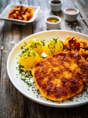Breaded fried pork chop with boiled potatoes and cabbage on wooden table
