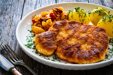 Breaded fried pork chop with boiled potatoes and cabbage on wooden table
