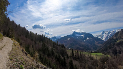 Fototapeta premium Scenic view of a hiking trail leading to the snow capped mountain peaks of Karawanks near Sinacher Gupf in Carinthia, Austria. Mount Wertatscha and Hochstuhl (Stol) is visible in early spring.Rosental
