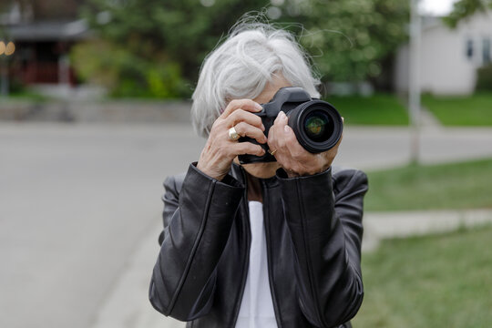 Portrait confident senior woman with digital camera on sidewalk