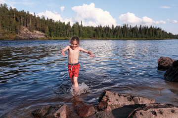 9-year-old curly boy runs in a river on a sunny summer day. Murmansk Oblast, Russia.