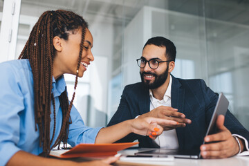 Cheerful multiracial colleagues discussing startup project and smiling during workday in office...
