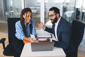 Successful male and female colleagues in formal clothes browsing website on modern cellular device using 4g wireless indoors, multicultural employees making online booking and banking via mobile app