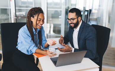 Cheerful male and female executive managers watching funny video on smartphone gadget using 4g wireless internet in office interior, successful professionals browsing banking application and laughing