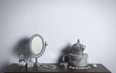 Small mirror, perfume bottles and jewelry on wooden table near light wall