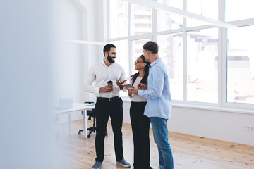 Fototapeta premium Diverse male and female colleagues in smart casual clothes discussing digital tablet options during office conversation about together brainstorming, successful partners talking during coffee break