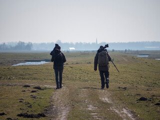 Birdwatchers with big cameras and backpacks walking in polder meadow landscape