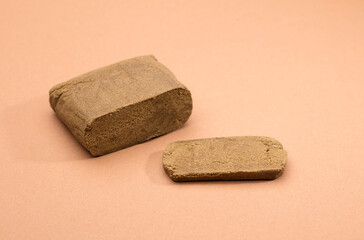 hashish tablet cut out next to large 100 gram portion, brown background - obrazy, fototapety, plakaty
