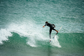 Young man in a black wetsuit surfing a wave with his board on the island of Lanzarote in the Canary...