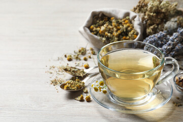 Glass cup of aromatic freshly brewed tea near different dry herbs on wooden table. Space for text