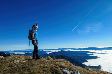 Woman with backpack hiking and admiring a scenic view from mount Eisenerzer Reichenstein in Styria, Austria, Europe. Ennstal valley is covered in clouds. Hiking trail, Wanderlust. Freedom concept