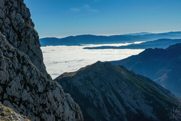 Obraz premium A massive cliff of mount Eisenerzer Reichenstein in Styria, Austria, Europe. Austrian Alps. Bare mountain ridges with view on the cloud covered Ennstal Valley. Hiking trail, Wanderlust. Sunny day