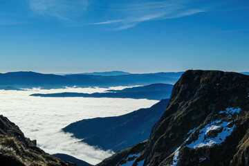 Distant hiker standing on a massive cliff near mount Eisenerzer Reichenstein in Styria, Austria, Europe. Austrian Alps. Bare mountain ridges with view on the cloud covered Ennstal Valley. Sunny day