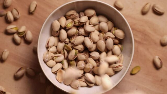 Pistachios falling into bowl, slow motion, top view. Filling bowl with nuts in shell.