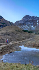 A woman in front of the frozen Krumpensee with a panoramic view on mount Eisenerzer Reichenstein in Styria, Austria, Europe. Austrian Alps.The valley is in the shadows,sunrise.Hiking trail,Wanderlust