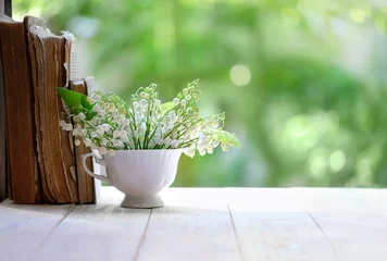 Fotobehang Lily of the valley in cup and books on white table, green natural background. symbol of spring season. beautiful romantic floral composition. copy space © Ju_see