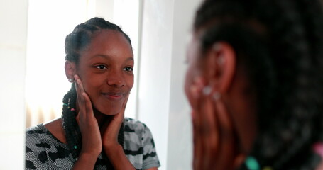 Confident black teen girl looking at herself in in mirror - Powered by Adobe