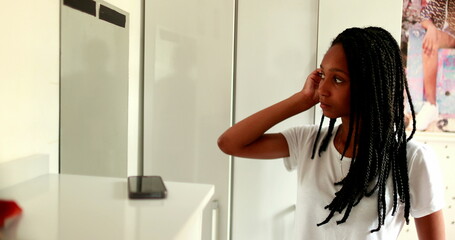 Fototapeta na wymiar Black teen girl looking at herself in front of mirror in room