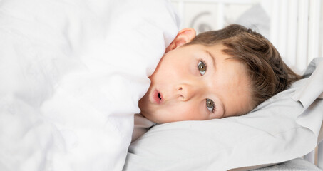 Portrait of playful little boy in bed. Daily regime concept