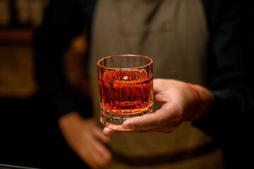 hand of bartender hold old-fashioned glass with alcoholic drink and a piece of ice