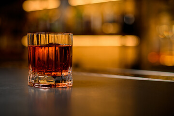 close-up of old-fashioned glass with alcoholic drink and piece of ice on blurred background