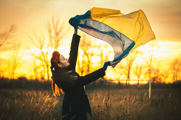 Sad young Ukrainian woman with the flag of Ukraine fluttering in the wind. The concept of...
