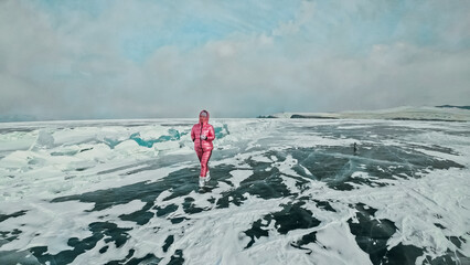 Girl walking on cracked ice of frozen lake Baikal. Woman traveler explores and looks at an ice...