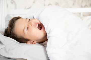 Fototapeta na wymiar Cute little boy wake up in his comfortable bed in the morning and yawns. Good morning