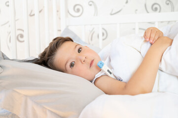 Sick cute boy lies in bed with a thermometer. Medicine concept