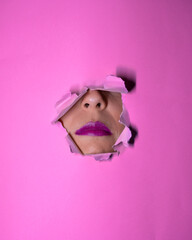 lips, eyes and face of a woman protruding through a pink cardboard