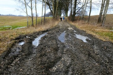 A dirt road with deep ruts and mud in early spring. Silhouettes of people walking.