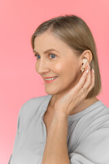 An old woman with Airpods on a pink-rose background. Close up. Portrait of an age woman.