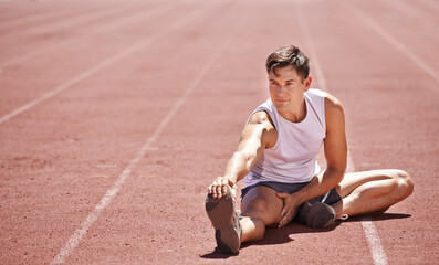 Preparing to win. Shot of an athlete stretching his legs while sitting on the track.