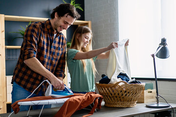 Happy father with daughter at home doing household chores and ironing together.