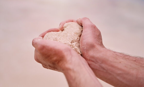 Summer is the season of love. Cropped shot of an unrecognizable man making a heart shape while holding sand on a beach.