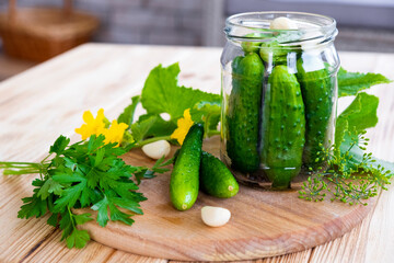Glass jar with fresh cucumbers, herbs, garlic, dill and parsley on wooden board. Cooking pickle cucumbers for home conservation.