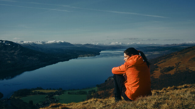 woman sat on the top of a mountain overlooking a loch